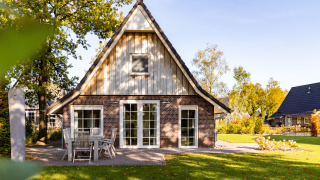 Wellness Lodge XL, una pequeña casa con fachada de ladrillo y madera, mesa al aire libre y césped verde.