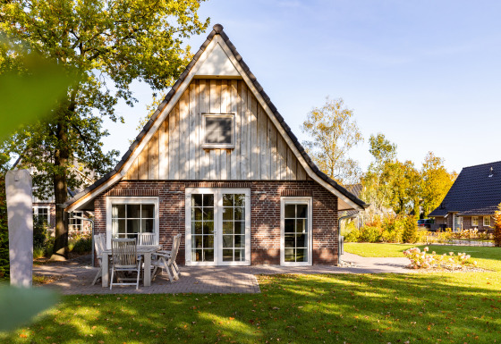 Wellness Lodge XL, una pequeña casa con fachada de ladrillo y madera, mesa al aire libre y césped verde.