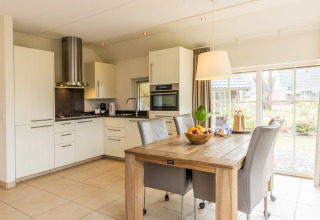 Cocina y comedor modernos y luminosos en Wellness Lodge XL en Hof van Salland, con grandes ventanales y mesa.