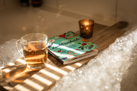Una taza de té y un libro sobre una bandeja de madera junto a una bañera en Wellness Lodge XL, Hof van Salland, Países Bajos.