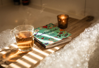 Eine Tasse Tee und ein Buch auf einem Tablett neben einer Badewanne im Wellness Lodge XL, Hof van Salland, Niederlande.