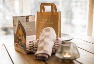 Willkommensgeschenk, Broschüre, Handtücher und Kerze auf Tisch in der Wellness Lodge XL, Hof van Salland.