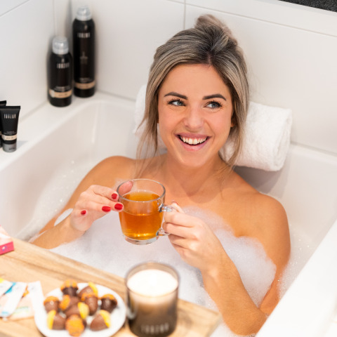 Mujer relajándose con té y bombones en una bañera en Wellness Lodge XL, Hof van Salland, Países Bajos.