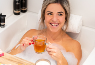 Frau entspannt sich mit Tee und Pralinen in einer Badewanne im Wellness Lodge XL, Hof van Salland, Niederlande.