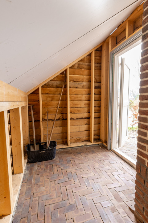 Innenaufnahme eines kleinen Hauses mit Ziegelfußboden, Dachschräge und Gartenwerkzeugen bei Hof van Salland.