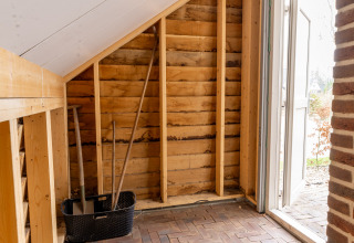 Innenaufnahme eines kleinen Hauses mit Ziegelfußboden, Dachschräge und Gartenwerkzeugen bei Hof van Salland.