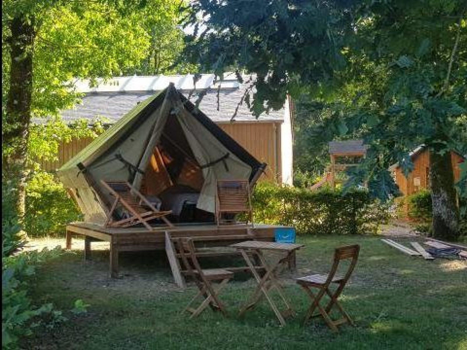 Safari Bivak-tent op houten platform met stoelen en tafel, onder bomen op een groene camping.