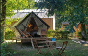 Safari Bivouac Tent on a wooden platform with chairs and table in the shade, surrounded by greenery.