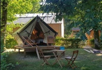 Safari Bivouac Tent on a wooden platform with chairs and table in the shade, surrounded by greenery.