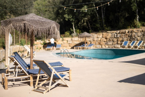Ontspanningszone aan het zwembad van Can Bora Lodges in Catalonië, Spanje, met ligstoelen en rieten parasols.