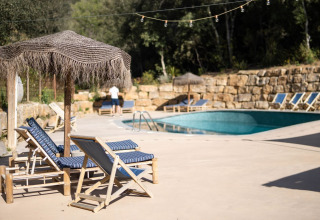 Ontspanningszone aan het zwembad van Can Bora Lodges in Catalonië, Spanje, met ligstoelen en rieten parasols.
