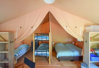 Interior de una tienda safari en Domaine Les 2 Soleils, Francia, con camas, estanterías y decoración rústica.