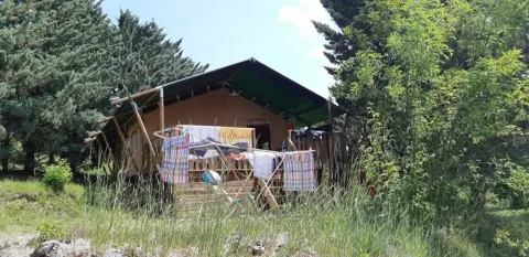 Safaritent bij Domaine Les 2 Soleils in Frankrijk, omringd door bomen en wasgoed dat buiten hangt te drogen.