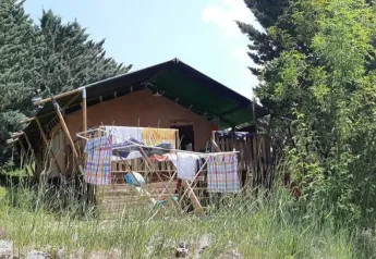 Tienda de safari en Domaine Les 2 Soleils, Francia, rodeada de árboles y ropa de colores secándose afuera.