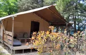 Safaritent Lodgetent met badkamer op Camping Luna del Monte in Italië, omringd door bomen en struiken.