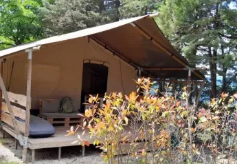 Safaritent Lodgetent met badkamer bij Camping Luna del Monte in Italië, omringd door bomen en struiken.