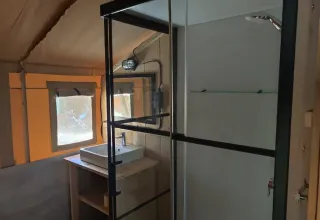 Interieur van Lodgetent met badkamer bij Camping Luna del Monte, Italië, met wastafel en douche.