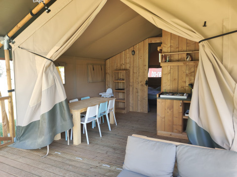 Interieur van een safari lodgetent met badkamer, eettafel, stoelen en gezellige zithoek.