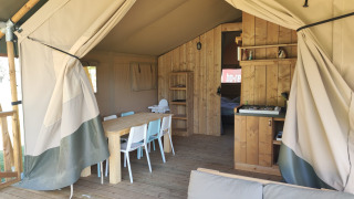 Innenansicht eines Safari-Lodgezeltes mit Badezimmer, Esstisch, Stühlen und gemütlichem Sofa.