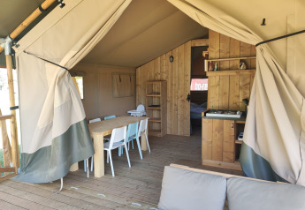 Interieur van een safari lodgetent met badkamer, eettafel, stoelen en gezellige zithoek.