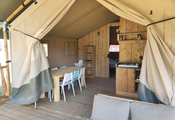 Interieur van een safari lodgetent met badkamer, eettafel, stoelen en gezellige zithoek.