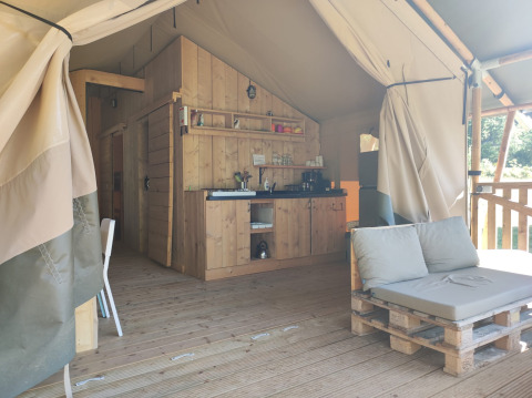Interieur van safaritent met houten kitchenette en palletbank bij Lodgetent met badkamer, Camping Luna del Monte, Italië.