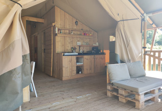 Interieur van safaritent met houten kitchenette en palletbank bij Lodgetent met badkamer, Camping Luna del Monte, Italië.
