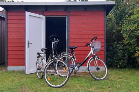 Twee fietsen staan geparkeerd voor een rood schuurtje met open deur bij lodge «Am Strand» in Duitsland.