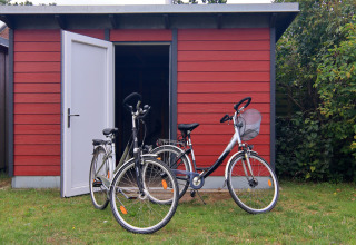 Twee fietsen staan geparkeerd voor een rood schuurtje met open deur bij lodge «Am Strand» in Duitsland.