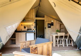 Interior of a safari glamping tent at Campsite Mareveld in the Netherlands, featuring a kitchenette and wood furniture.