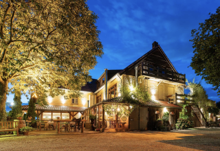Evening view of Campsite Mareveld in Limburg, Netherlands, featuring a warmly lit building and outdoor seating.