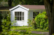 White chalet at Campsite Mareveld in the Netherlands, surrounded by lush greenery and trees in sunlight.