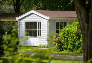 White chalet at Campsite Mareveld in the Netherlands, surrounded by lush greenery and trees in sunlight.