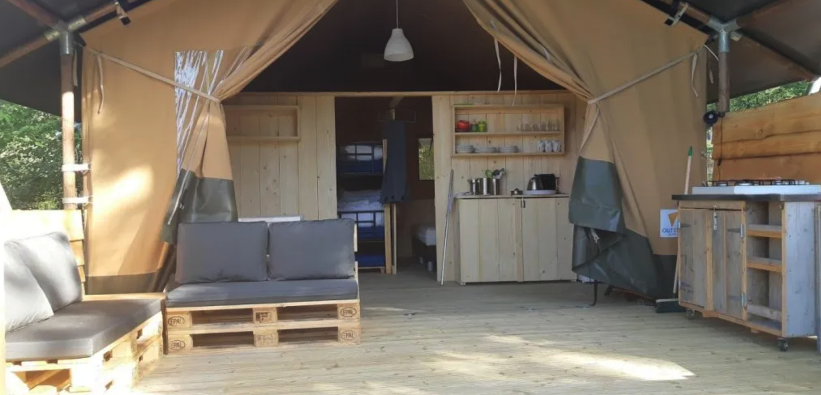 Interieur van een safaritent op Camping Moulin de Chaules in Frankrijk met palletbanken en keukentje.