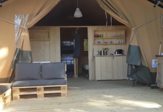 Interior de una tienda safari en Camping Moulin de Chaules, Francia, con suelos de madera y cocina básica.