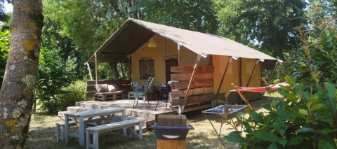 Tente safari au Camping Moulin de Chaules en France, terrasse avec bancs, barbecue et espaces verts.