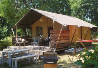 Tente safari au Camping Moulin de Chaules en France, terrasse avec bancs, barbecue et espaces verts.