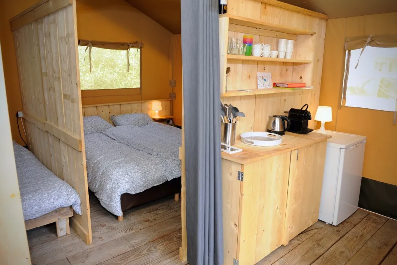 Binnenaanzicht van de safaritent bij Camping Moulin de Chaules in Frankrijk met slaapkamer en kitchenette.