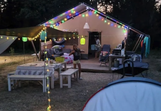 Campamento con tienda safari, luces de colores y área de comedor en Camping Moulin de Chaules, Francia.
