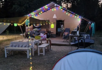Campamento con tienda safari, luces de colores y área de comedor en Camping Moulin de Chaules, Francia.