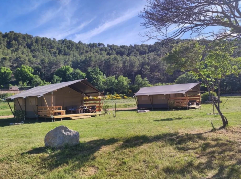 Deux tentes safari au Camping Moulin de Chaules en France, entourées de nature et d’arbres verdoyants.