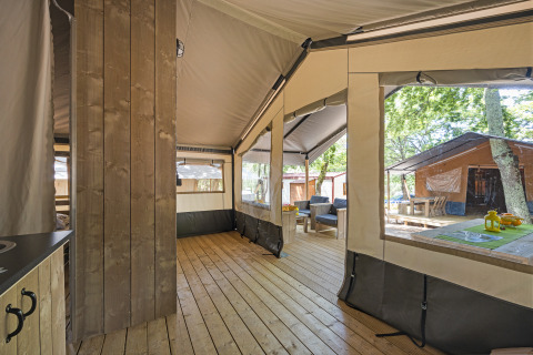 Vista interna di una tenda safari con pavimento in legno, area salotto e tavolo al Camping Aminess Maravea, Croazia.