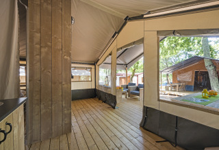 Vista interna di una tenda safari con pavimento in legno, area salotto e tavolo al Camping Aminess Maravea, Croazia.
