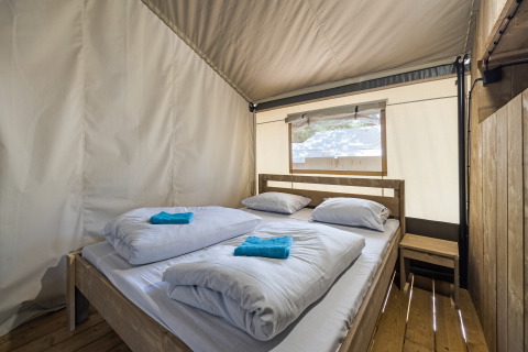 Interno di una tenda safari con letto matrimoniale, lenzuola e finestra al Camping Aminess Maravea in Croazia.