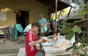 Zwei Jungen essen an einem Holztisch vor einem Safarizelt, umgeben von Bäumen und Camping-Atmosphäre.