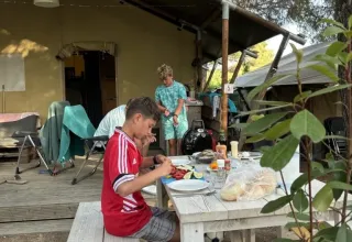 Zwei Jungen essen an einem Holztisch vor einem Safarizelt, umgeben von Bäumen und Camping-Atmosphäre.