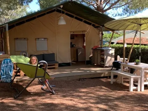 Ein Mädchen entspannt vor einem Safarizelt auf dem Campingplatz Casa dei Prati mit Sitzbereich in Italien.