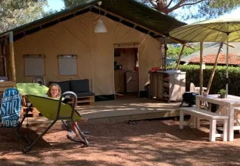 Ein Mädchen entspannt vor einem Safarizelt auf dem Campingplatz Casa dei Prati mit Sitzbereich in Italien.