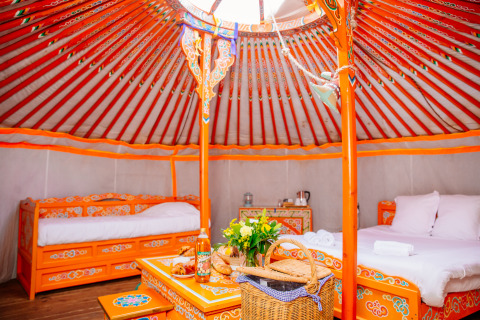 Interior de una yurta colorida con camas y mesa en Domaine EcÔtelia, Francia, estilo glamping acogedor.