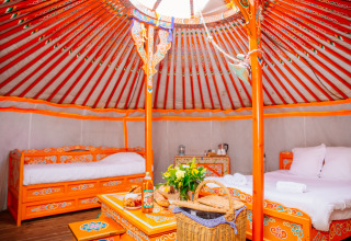 Bunte, traditionell eingerichtete Jurte mit Betten und Tisch in Domaine EcÔtelia, Frankreich, Glamping-Stil.